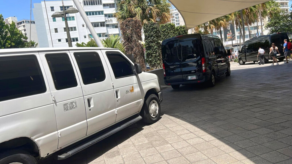 White taxi van and black passenger shuttles lined up outside a hotel in San Juan, Puerto Rico.